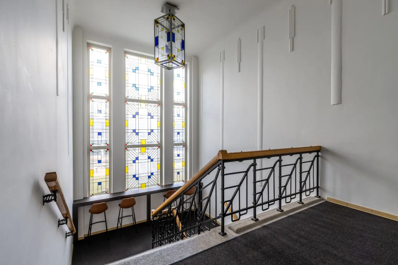 Trapportaal met glas-in-loodramen en zitgedeelte in het gebouw aan de Lage Naarderweg.